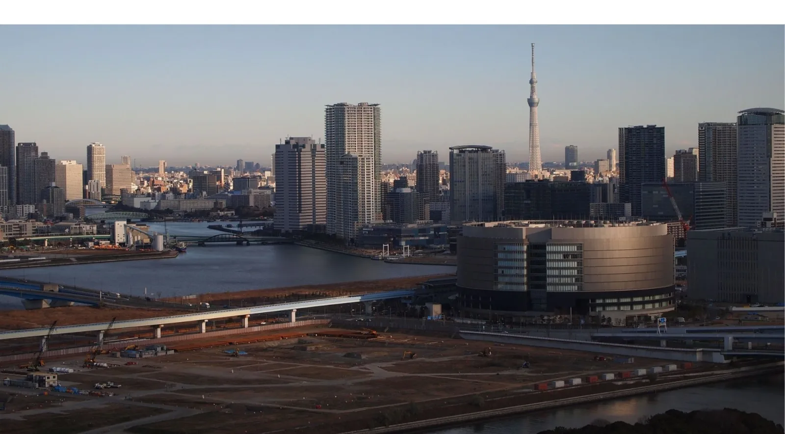 Aerial view of Toyosu Market's circular building with Tokyo Skytree visible in the background at dusk